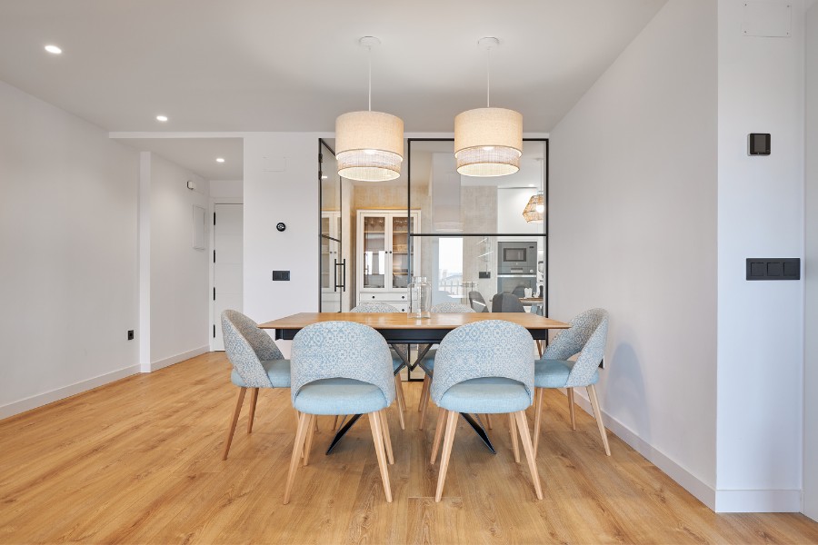 comedor reformado en madrid con suelo de madera, sillas tapizadas y luminarias colgantes modernas